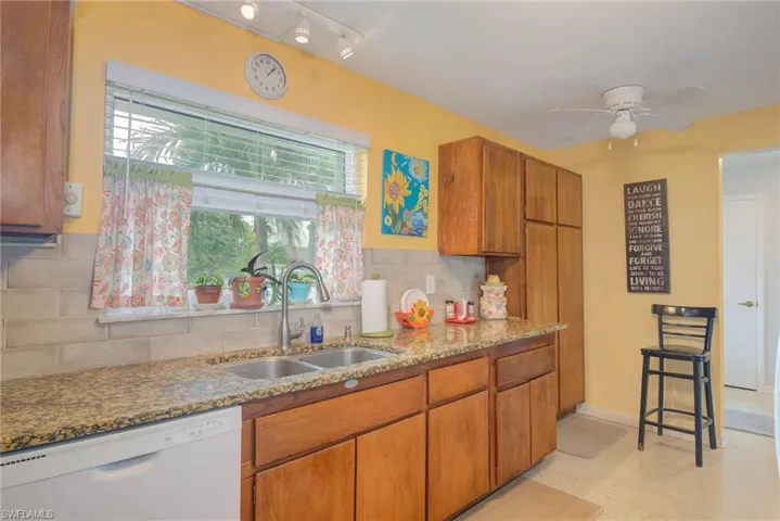 Kitchen with brown cabinets, dishwasher, light stone counters, ceiling fan, and decorative backsplash