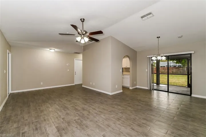 Unfurnished room with ceiling fan with notable chandelier, vaulted ceiling, and dark hardwood / wood-style floors