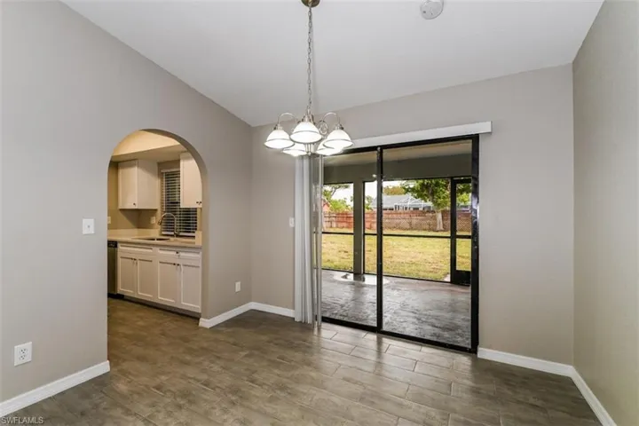 Unfurnished dining area featuring dark wood-type flooring, lofted ceiling, sink, and a notable chandelier