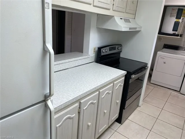 Kitchen featuring freestanding refrigerator, stainless steel range with electric stovetop, washer / dryer, light countertops, and electric water heater