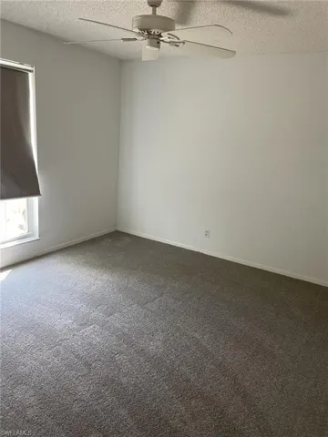 Empty room with a ceiling fan, dark carpet, and a textured ceiling