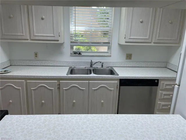 Kitchen featuring light countertops, stainless steel dishwasher, freestanding refrigerator, and white cabinetry