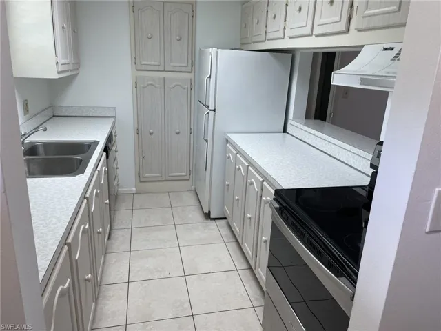 Kitchen featuring range with electric stovetop, light countertops, exhaust hood, light tile patterned floors, and freestanding refrigerator