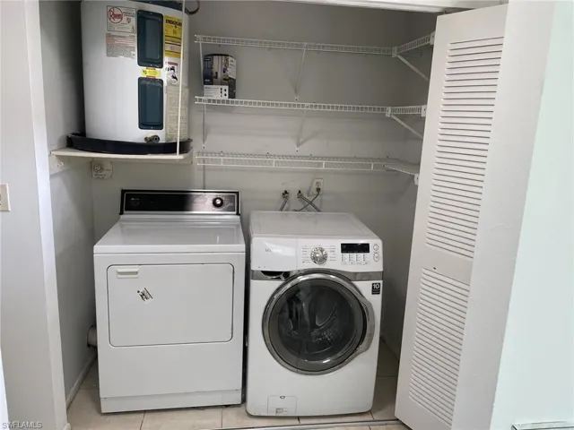 Laundry room featuring electric water heater, light tile patterned flooring, and separate washer and dryer