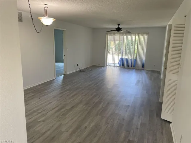 Unfurnished living room featuring dark wood-type flooring, a textured ceiling, and ceiling fan