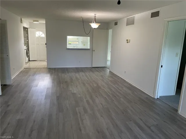 Unfurnished living room featuring a textured ceiling, dark wood-style flooring, and washer / dryer
