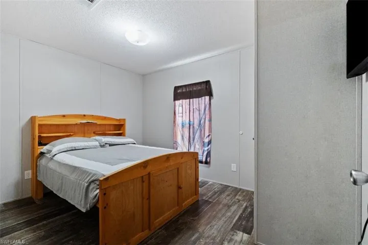 Bedroom with dark wood-style floors, a textured ceiling, and a decorative wall