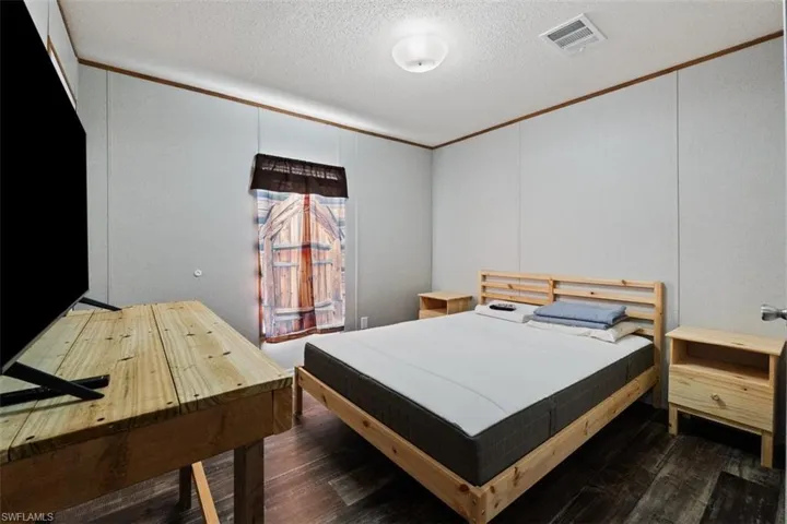 Bedroom featuring hardwood / wood-style flooring, ornamental molding, a decorative wall, and a textured ceiling