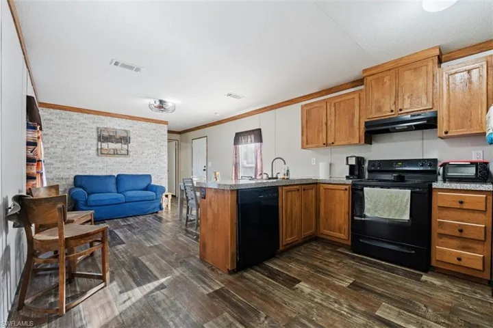 Kitchen with a peninsula, black appliances, brown cabinetry, open floor plan, and crown molding