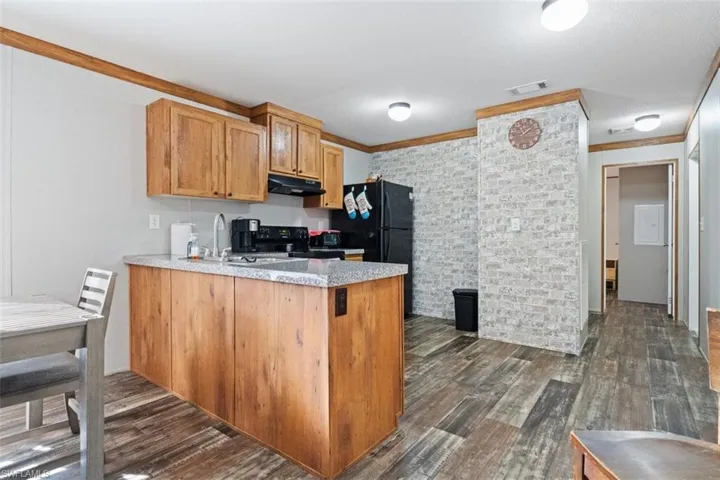 Kitchen with a peninsula, dark wood finished floors, black appliances, light stone countertops, and ornamental molding