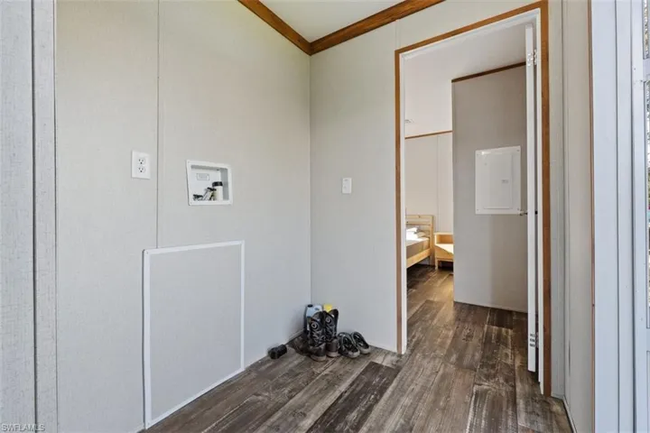 Laundry room with dark wood-style floors, ornamental molding, hookup for a washing machine, and electric panel