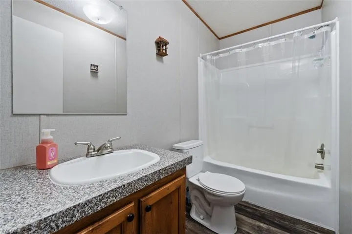 Bathroom with shower / bathtub combination with curtain, dark wood-type flooring, and vanity