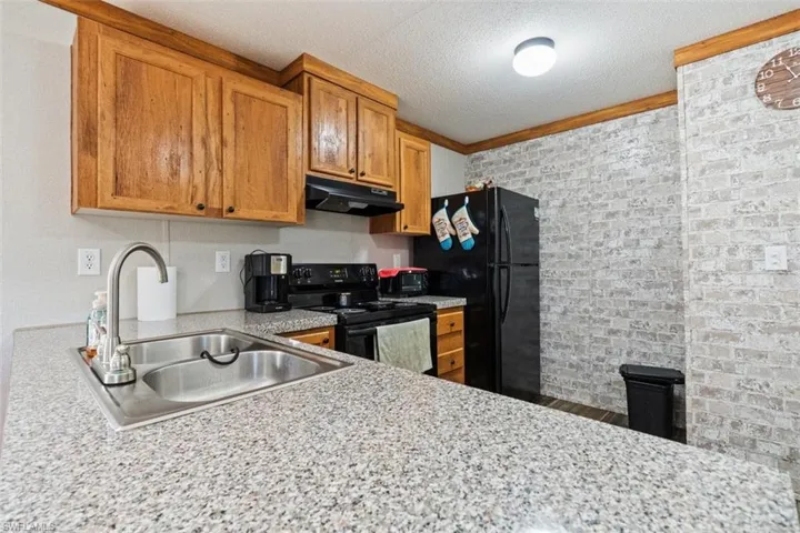 Kitchen with black appliances, a textured ceiling, under cabinet range hood, ornamental molding, and brown cabinetry
