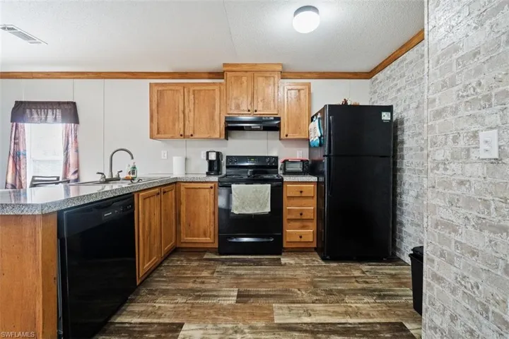 Kitchen with brick wall, black appliances, a textured ceiling, dark wood-style flooring, and brown cabinetry
