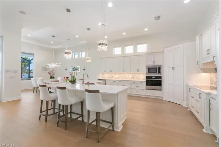 Kitchen with appliances with stainless steel finishes, sink, white cabinets, hanging light fixtures, and a large island