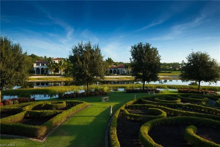 The property features a meticulously maintained garden with sculpted hedges and a lush lawn, overlooking a serene body of water