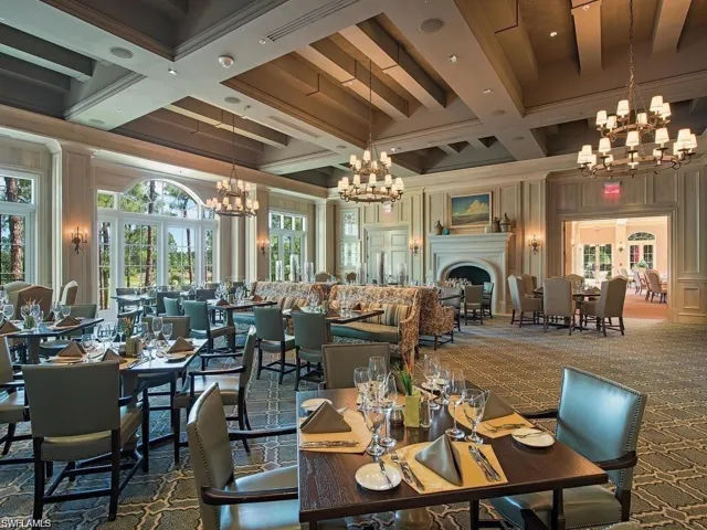 This dining area features a coffered ceiling, elegant chandeliers, and large windows with arched transoms that provide views of trees