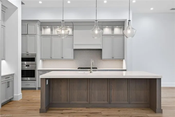 Kitchen features two tone cabinets, pretty glass pendant lights and light wood floors