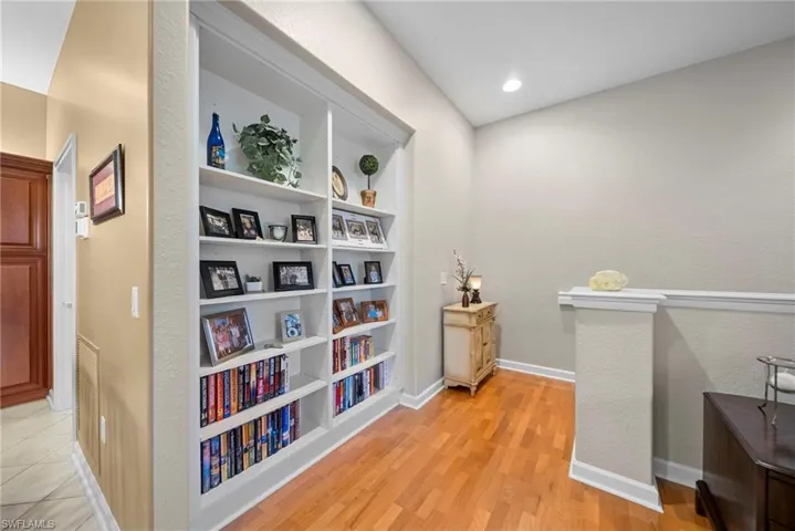 Corridor featuring built in features, a textured wall, light wood-type flooring, and recessed lighting