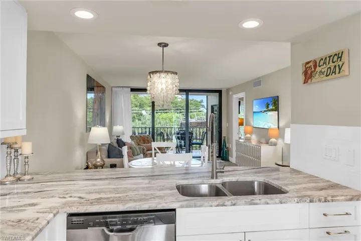 Kitchen featuring stainless steel dishwasher, a sink, light stone countertops, a chandelier, and white cabinetry