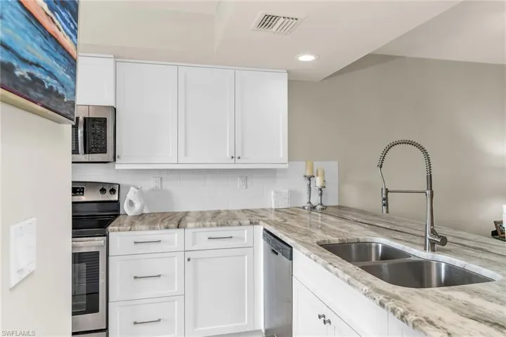 Kitchen with stainless steel appliances, a sink, decorative backsplash, light stone countertops, and recessed lighting