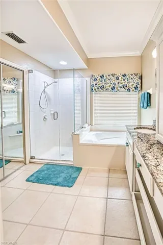 Bathroom featuring vanity, a garden tub, a shower stall, crown molding, and light tile patterned flooring