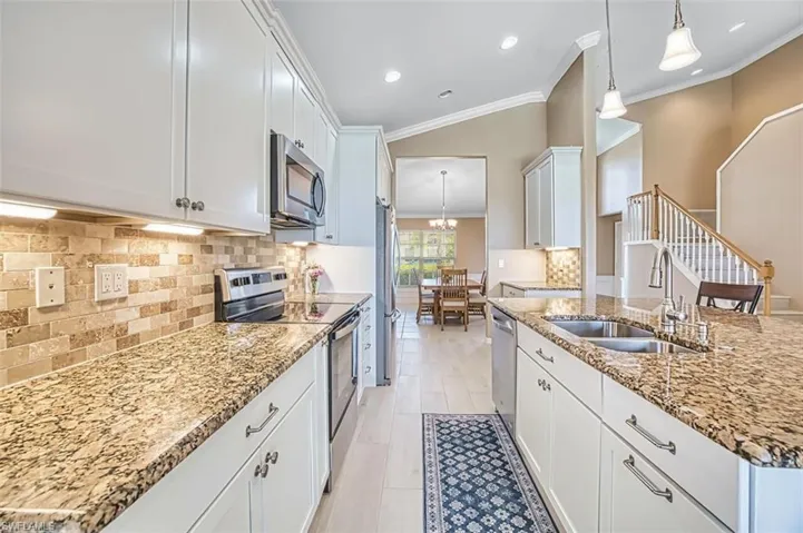 Kitchen with stainless steel appliances, tasteful backsplash, white cabinets, lofted ceiling, and ornamental molding