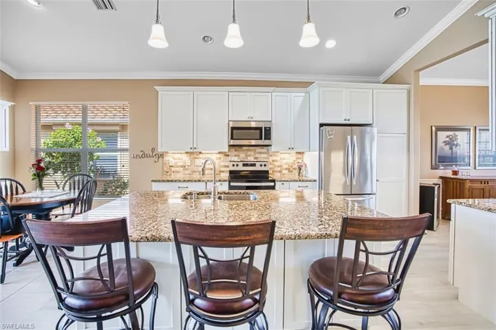 Kitchen with white cabinets, stainless steel appliances, ornamental molding, light stone counters, and a center island with sink