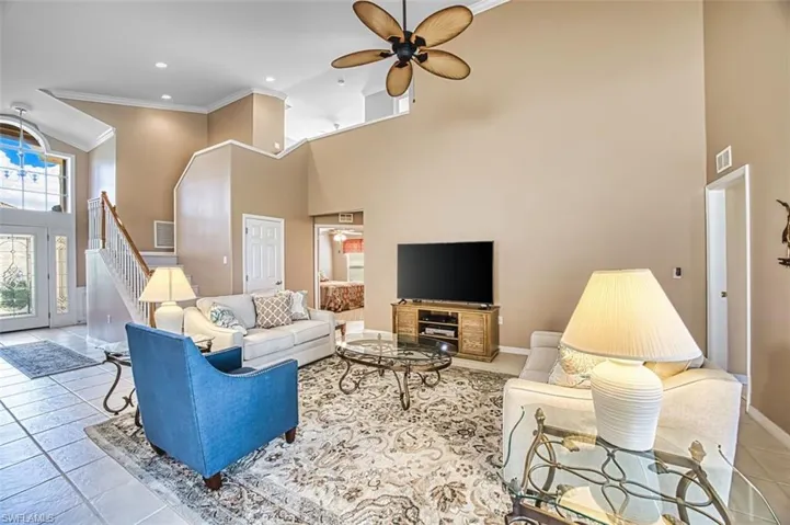 Tiled living area with crown molding, a high ceiling, ceiling fan, and recessed lighting