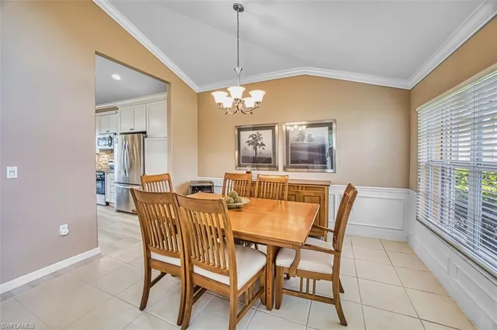 Dining space featuring vaulted ceiling, ornamental molding, suspended lighting, light tile patterned floors, and wainscoting