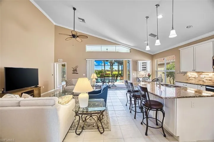 Living area with crown molding, vaulted ceiling, a sunroom, light tile patterned floors, and a ceiling fan