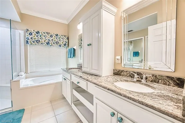 Full bathroom with double vanity, a garden tub, ornamental molding, light tile patterned floors, and a stall shower