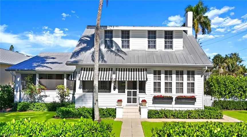 View of front of home with a metal roof, a sunroom, a chimney, a front yard, and entry steps