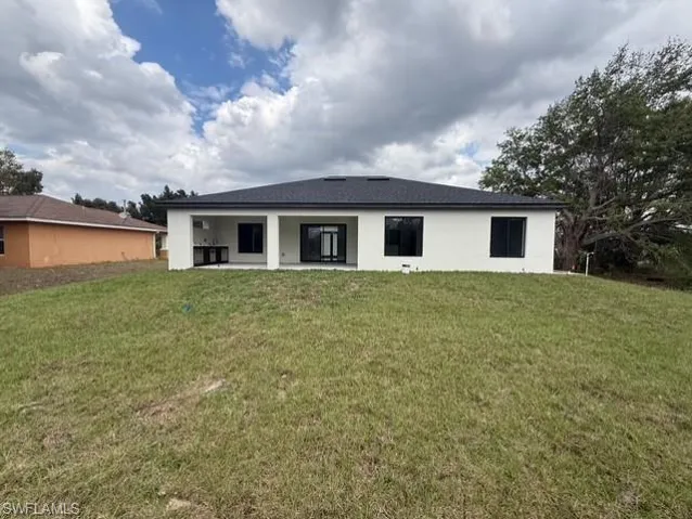 Rear view of house with a lawn, a patio, and stucco siding