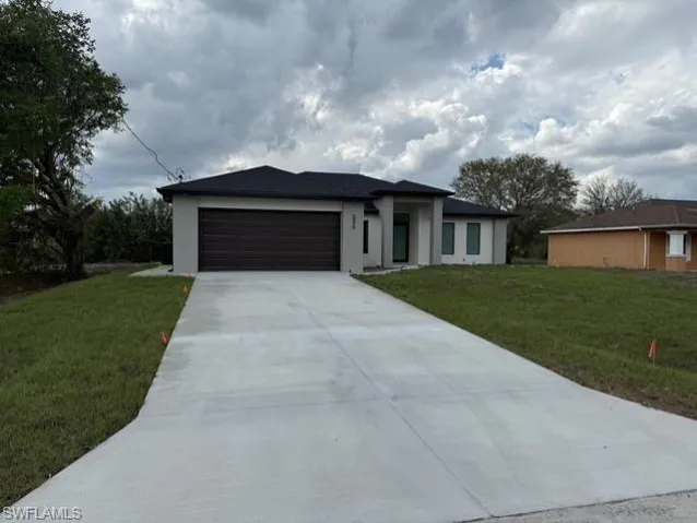 View of front facade featuring a front lawn, a garage, driveway, and stucco siding
