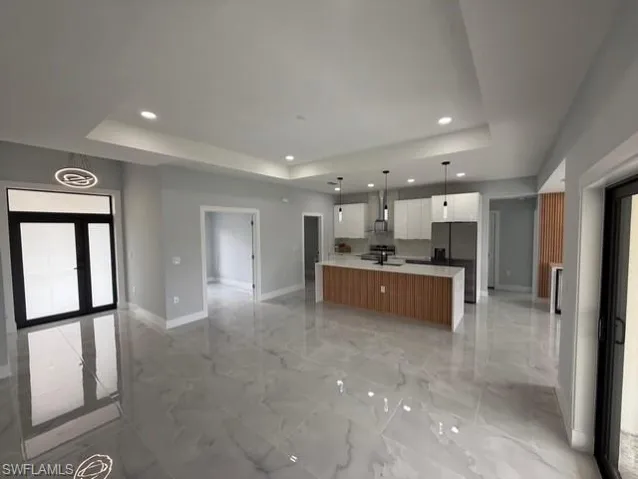 Kitchen featuring open floor plan, a large island, white cabinets, hanging light fixtures, and a raised ceiling