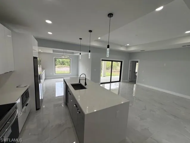 Kitchen featuring stainless steel appliances, a spacious island, light stone counters, open floor plan, and modern cabinets