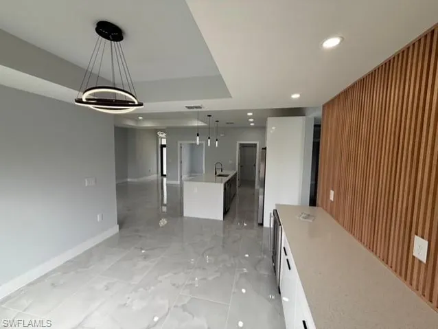 Kitchen featuring pendant lighting, a large island, light stone countertops, white cabinetry, and wooden walls