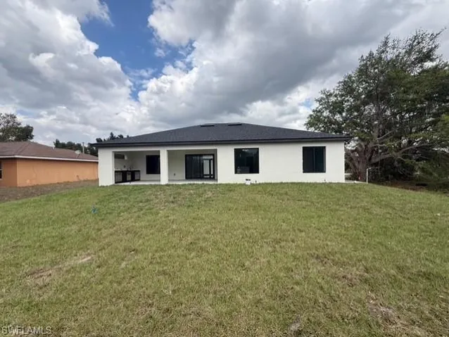 Rear view of house with a yard, a patio area, and stucco siding