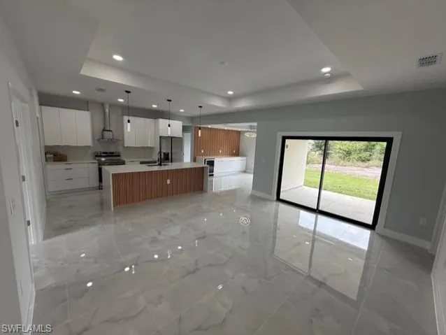 Kitchen with open floor plan, an island with sink, stainless steel appliances, a tray ceiling, and hanging light fixtures
