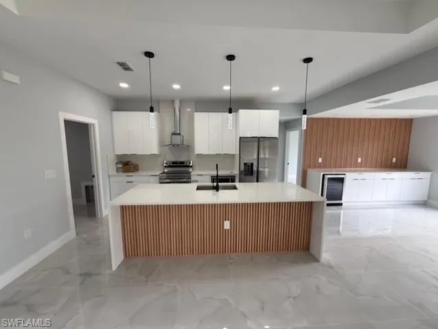 Kitchen featuring white cabinets, hanging light fixtures, stainless steel appliances, and a large island with sink