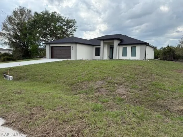 Prairie-style home featuring a front lawn, a garage, driveway, and stucco siding