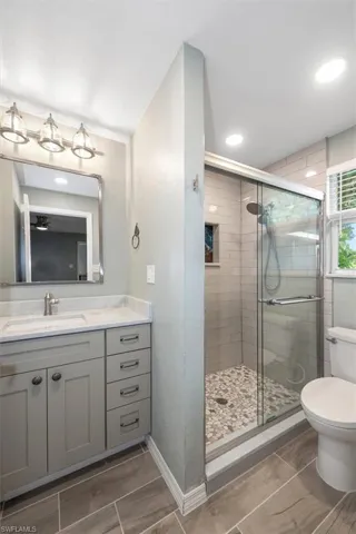 Bathroom with toilet, vanity, a stall shower, wood finish floors, and baseboards