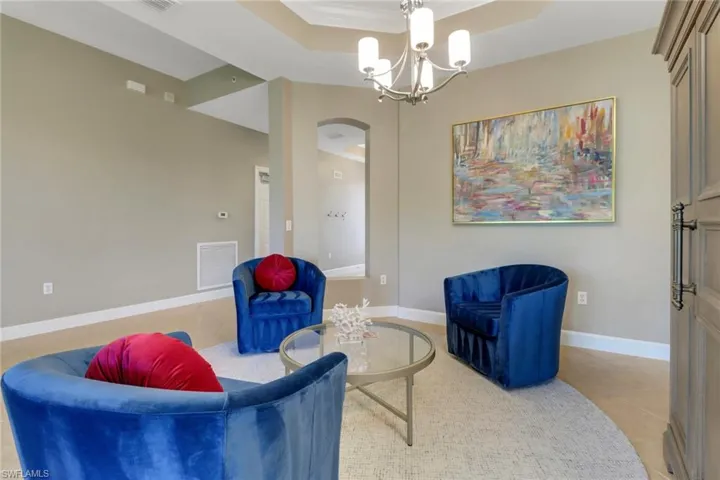 Living area with light tile patterned floors, visible vents, a raised ceiling, arched walkways, and a chandelier