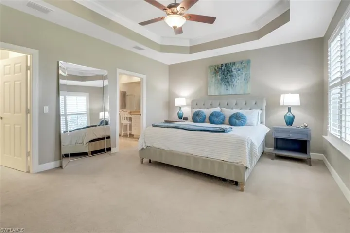 Bedroom with crown molding, visible vents, baseboards, a raised ceiling, and light colored carpet
