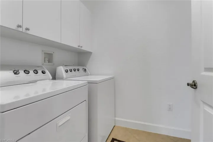 Laundry area with baseboards, washing machine and dryer, light tile patterned flooring, and cabinet space