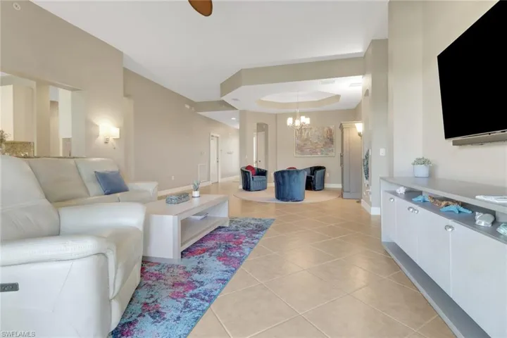 Living area with light tile patterned floors, a raised ceiling, a notable chandelier, and baseboards
