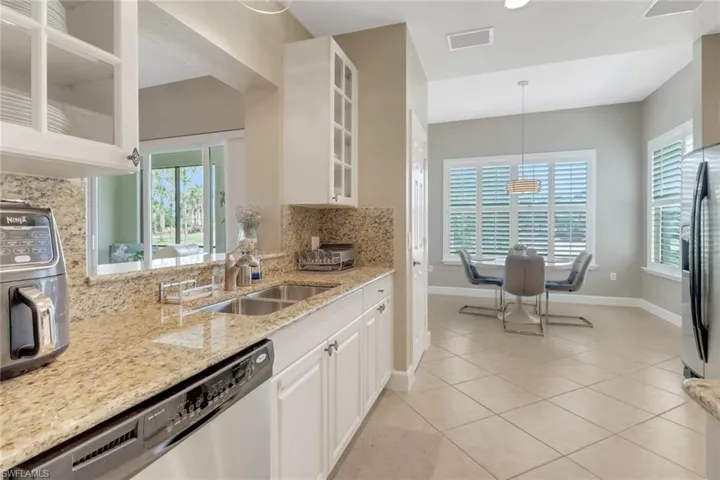 Kitchen with stainless steel appliances, backsplash, glass insert cabinets, light stone countertops, and baseboards