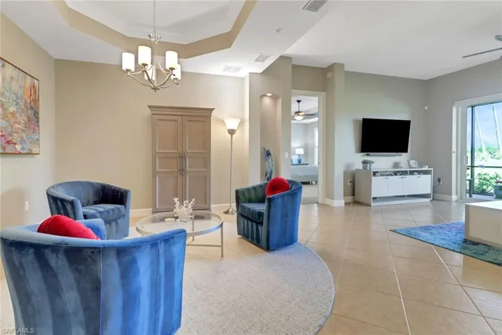 Living room featuring light tile patterned floors, a tray ceiling, a notable chandelier, visible vents, and baseboards
