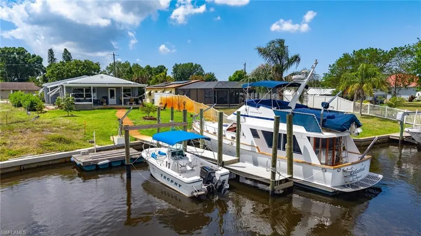 View of dock featuring boat lift, fence, a water view, and a lawn